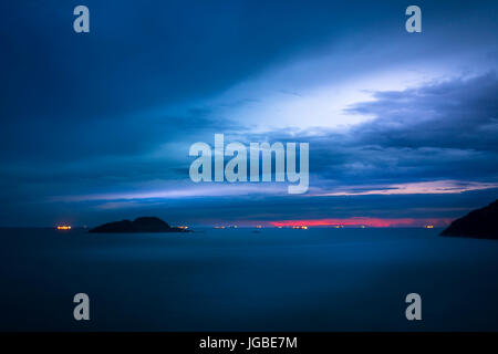 Sunset on the beach, islands and ships with lights on, late in the day with cloudy sky. Stock Photo