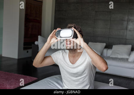 Amazed man with virtual reality headset sitting at home Stock Photo