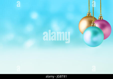 Three Christmas baubles in turquoise, pink and gold, hanging at different lengths in a group against a soft bokeh background of turquoise and white, w Stock Photo