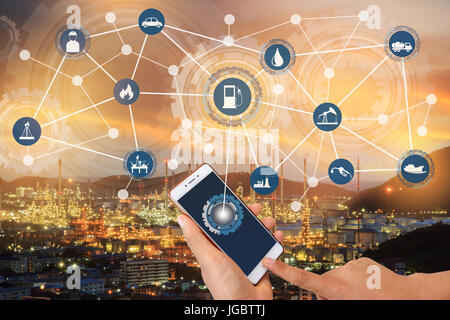 Industry 4.0 connect hand holding smartphone and industrial icons on oil refinery industry sunset background. Stock Photo