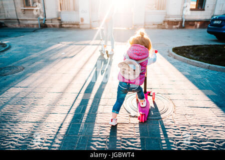 Little girl with blonde hair rides on scooter Stock Photo