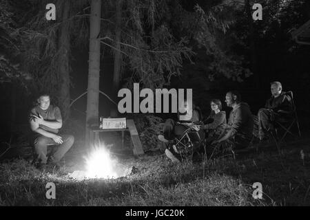 TUKLEKY, CZECH REPUBLIC - JULY 1, 2017: Group of adults around a fire pit in woods at night on July 1, 2017 in Tukleky village, Vysocina Region. Stock Photo