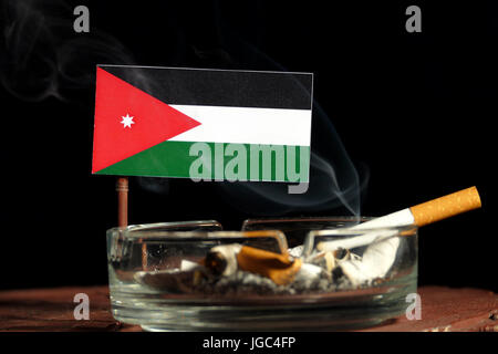 Jordanian flag with burning cigarette in ashtray isolated on black background Stock Photo