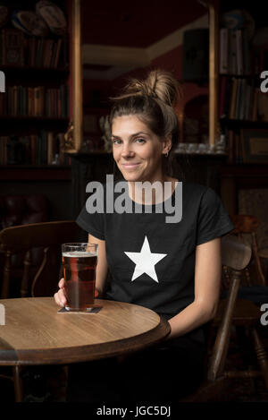 A modern young woman drinking real ale in a London pub Stock Photo