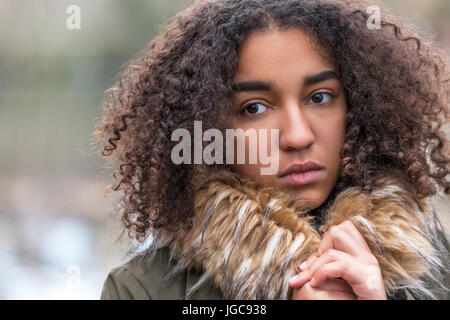 Beautiful mixed race African American girl teenager female young woman outside wearing fake fur collar coat looking sad depressed or thoughtful Stock Photo
