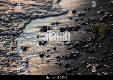 A close shot of water on a lake shore, with details of sands and little stones Stock Photo