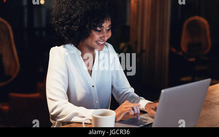 Happy young woman working at the laptop late at night. African business woman working overtime in the office. Stock Photo