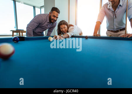 Young men and woman taking a break from work. businesswoman playing billiards at office while her colleagues look on. Stock Photo