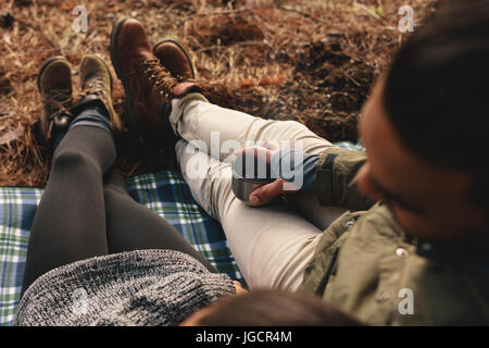 Close up of young couple sitting together outdoors, focus on hands holding cup of coffee. Hikers relaxing on mountain slope. Stock Photo