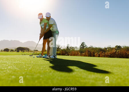 Male golf instructor teaching female golf player, personal trainer giving lesson on golf course. Male showing woman to play golf. Stock Photo