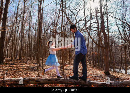 Father and daughter holding hands standing on a tree trunk in the forest Stock Photo