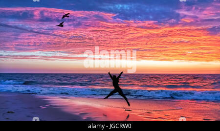 Silhouette of a woman Jumping  on the beach at sunset, Australia Stock Photo