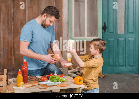 side view of dad and son cooking meat burgers together Stock Photo