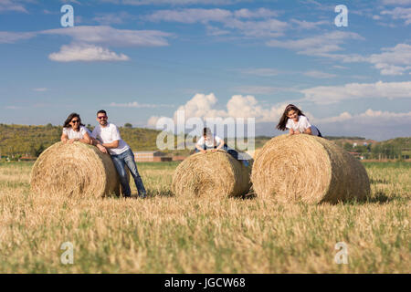 Family leaning on hay bales on in a field Stock Photo