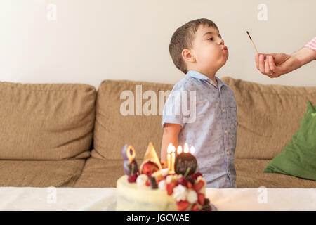 Boy blowing out a match after his mother has lit candles on a birthday cake Stock Photo