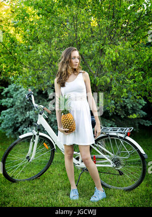 Portrait of a woman by her bicycle holding a pineapple Stock Photo