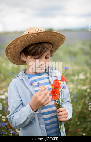 Boy standing in a field of wildflowers holding a bunch of flowers Stock Photo