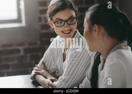 two attractive multicultural businesswomen talking while sitting in modern office