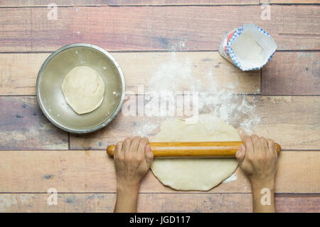 stretching dough with rolling pin on wooden table for cooking Stock Photo