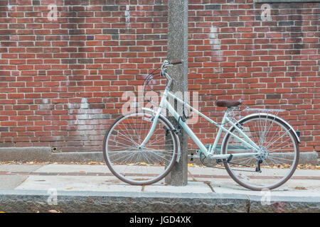 Bicycle locked up to a concrete post next to a brick wall. Stock Photo
