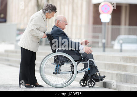 senior man in wheelchair being pushed by wife Stock Photo
