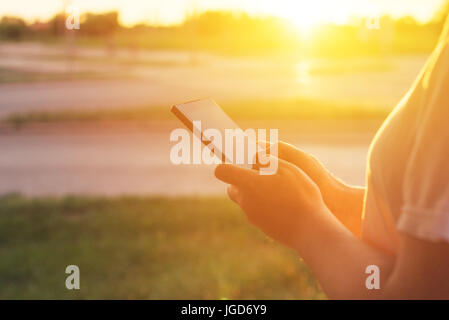 Using mobile phone on the street in morning, woman typing message on smartphone during sunrise Stock Photo
