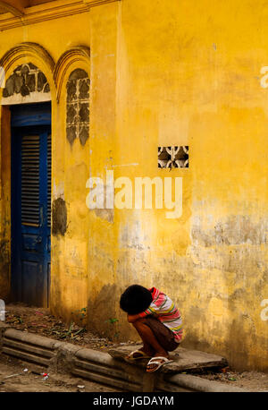 A Khmer boy sits outside an old building in Phnom Penh, Cambodia Stock Photo