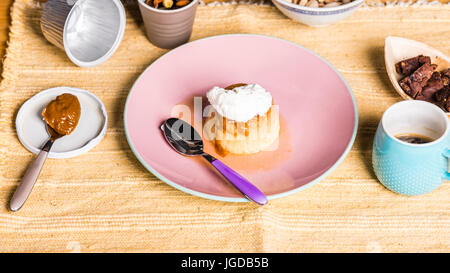 Flan -  creme on top, on a pink plate over a wooden board, served with chocolate cookies, dulce de leche confection , coffee and nuts. Stock Photo