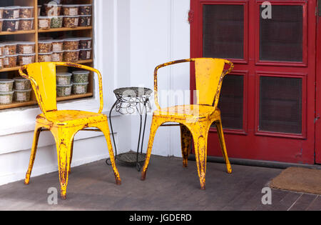 Two colorful yellow weathered metal chairs on a porch set against a red door. Stock Photo