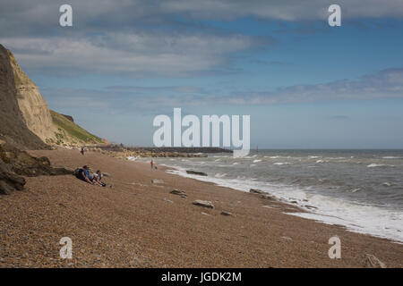 Costal seaside view with cliffs and people on a cloudy day across pebble shore line of Eype beach, Symmondsbury, near Bridport, Dorset, UK. Stock Photo