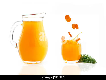 fresh sliced carrots falling in a glass with juice in a  a jug on a white isolated background Stock Photo
