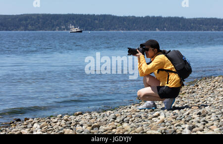 Woman photographer taking photos from shoreline during bright summer day Stock Photo