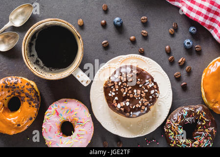 Glazed donuts and cup of black coffee espresso on stone background. Top view. Flat lay composition with food