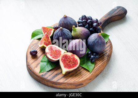 Fresh figs and grapes on wooden cutting board on bright gray background. Snack set for cheese and wine Stock Photo