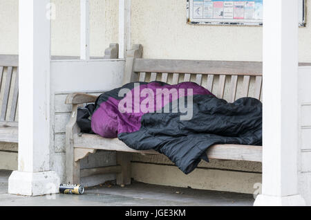 Sleeping rough on the streets. Homeless person sleeping on a bench in the UK.