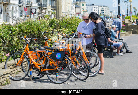 Bicycle rental. Couple using the Donkey Republic app on a smartphone to hire bicycles in Worthing, West Sussex, England, UK. Stock Photo