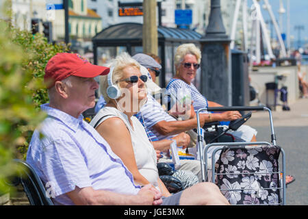 Elderly woman sitting outside listening to music on headphones in Summer. Stock Photo