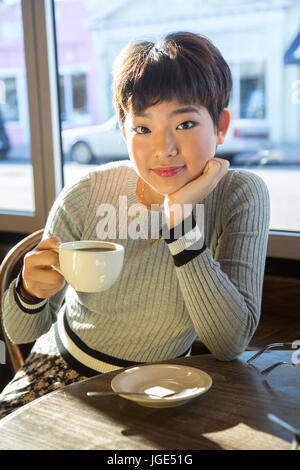 Serious Asian teenage girl drinking coffee in coffee shop