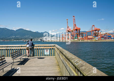 Couple looking at the water and mountains in the Vancouver harbour on the pier at Crab Park at the waterfront. Burrard Inlet. Stock Photo