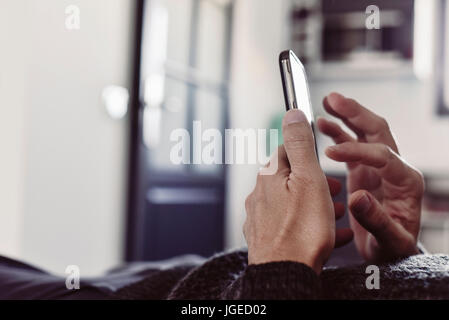 closeup of a young caucasian man using his smartphone lying down on a couch or a bed Stock Photo