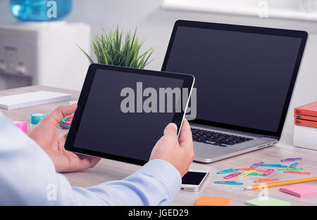 Businessman holding and working with digital tablet pc. Modern office desk workplace with laptop computer mockup and tablet pc mockup in man hands. Stock Photo