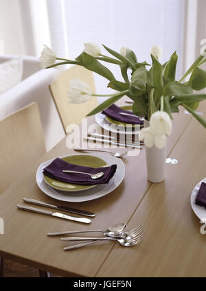Modern pale wood table setting with vase of tulips Stock Photo