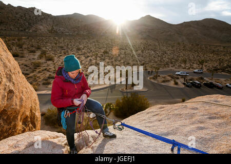 Young caucasian woman dressed for rock climbing adjusts her equipment in the desert at sunset Stock Photo