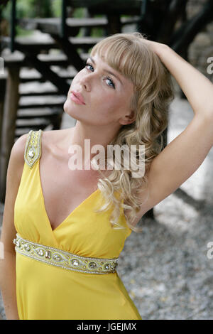 Beautiful blond female model in a fancy yellow cocktail dress enjoying good weather Stock Photo