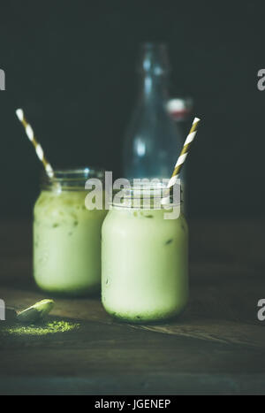Refreshing iced coconut matcha latte drink in jars, wooden table Stock Photo