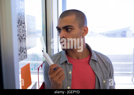 Male executive reading sticky notes on glass door in office Stock Photo