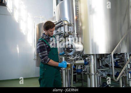 Male worker taking beer from storage tank while standing at factory Stock Photo