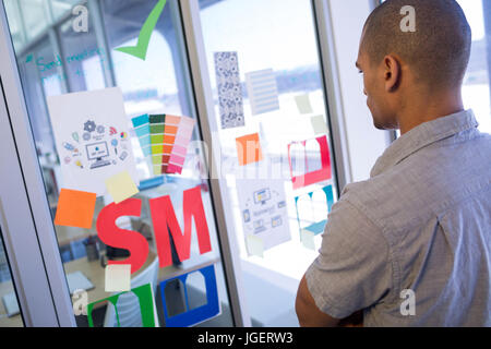 Male executive reading sticky notes on glass door in office Stock Photo