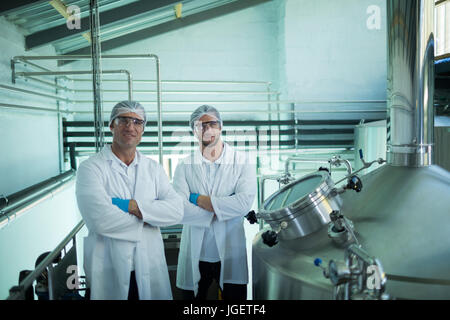 Portrait of scientists with arms crossed standing by storage tank in factory Stock Photo