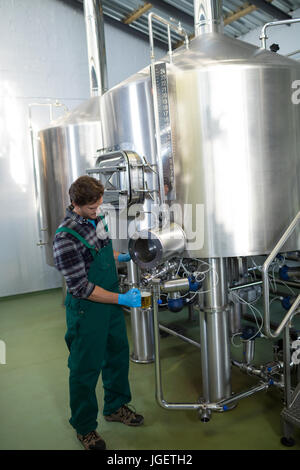 Male worker taking beer from storage tank at factory Stock Photo